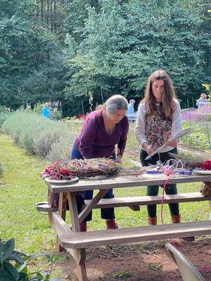 2 women making wreaths with lavender field behind them